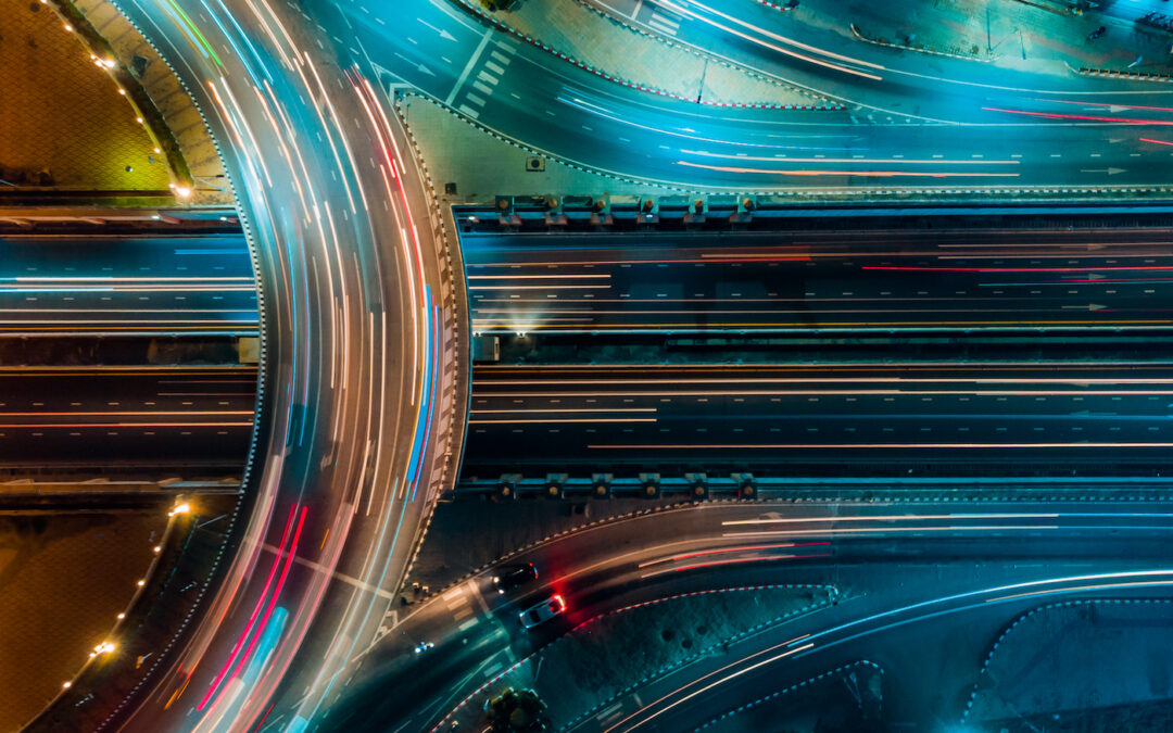 Aerial view of curving highways at night with streaks of light from moving vehicles, illustrating busy traffic flow, potentially related to hemp transportation logistics.